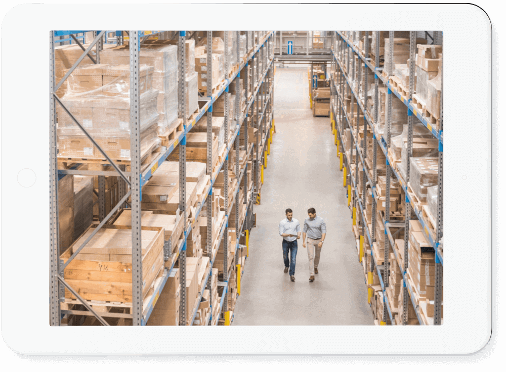 2 people walking down an aisle in a warehouse.